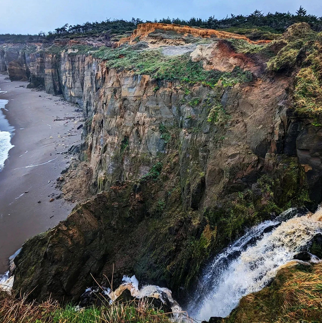 Waterfall at Blacklock Point Trail in Langlois, Oregon with a view of the ocean and sea cliffs.
