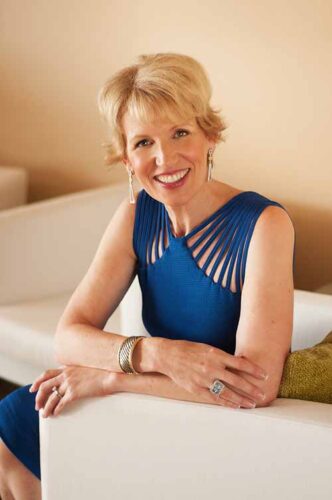 Mari Smith, Queen of Facebook, wearing a blue dress, sitting on a white sofa