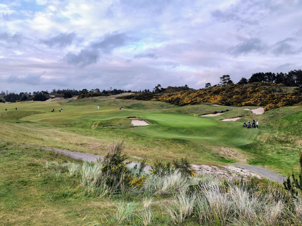 A beautiful view of a parkland area with a par 4 golf hole in Bandon, Oregon, with the ocean in the background and yellow heather in bloom