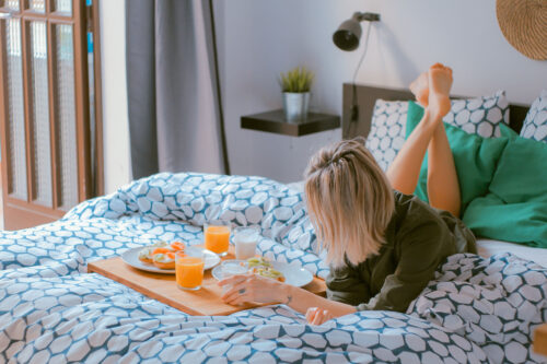 A woman lying on the bed with breakfast in bed and a book at a vacation rental on the Southern Oregon Coast